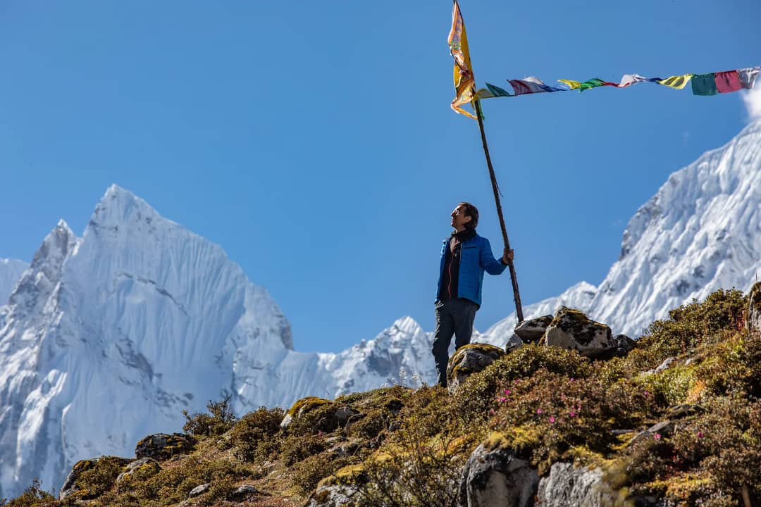 A man stands with prayer flags against the backdrop of snowcapped mountains in Nepal.