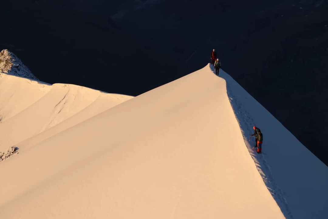 Adventurers climb a snowy peak at dawn, highlighting a thrilling winter landscape.