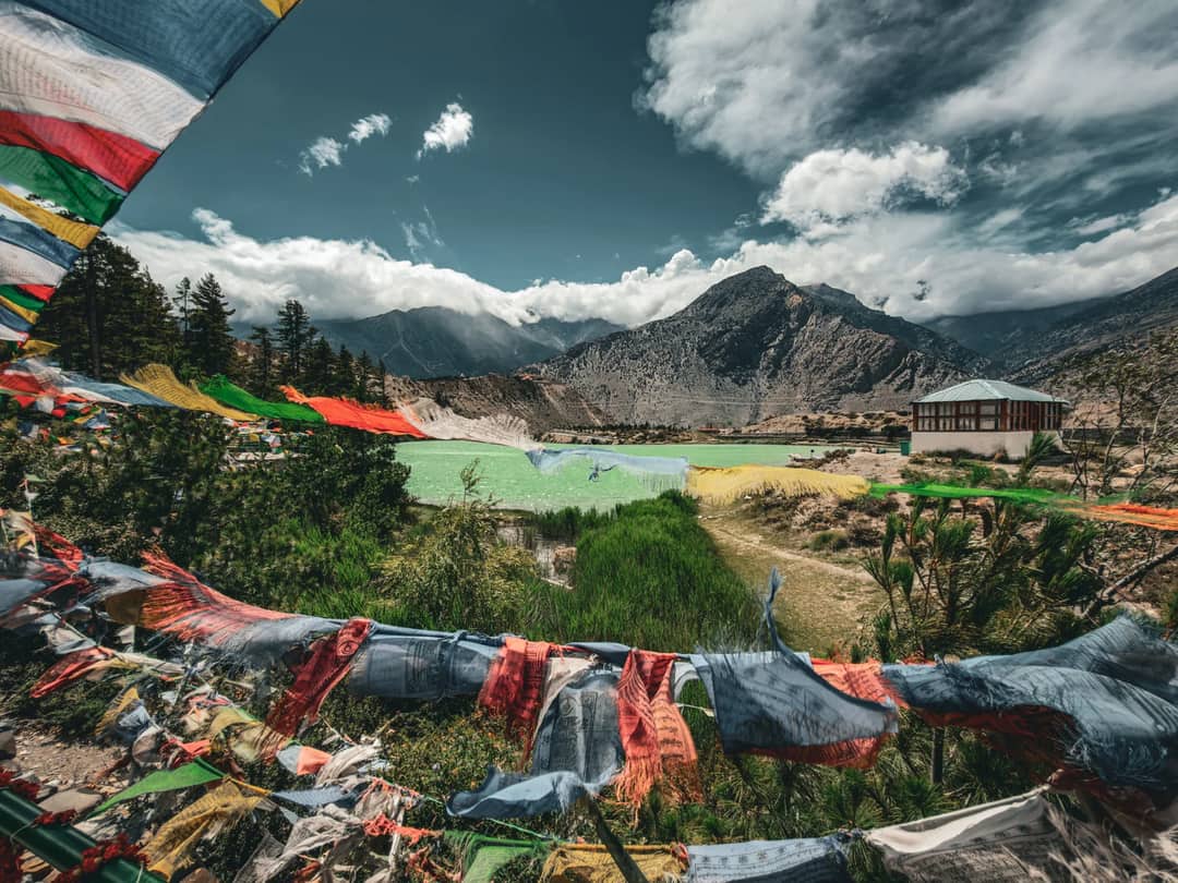 Colorful prayer flags in Jomsom, Nepal with mountains and a vibrant green landscape under a dramatic sky.
