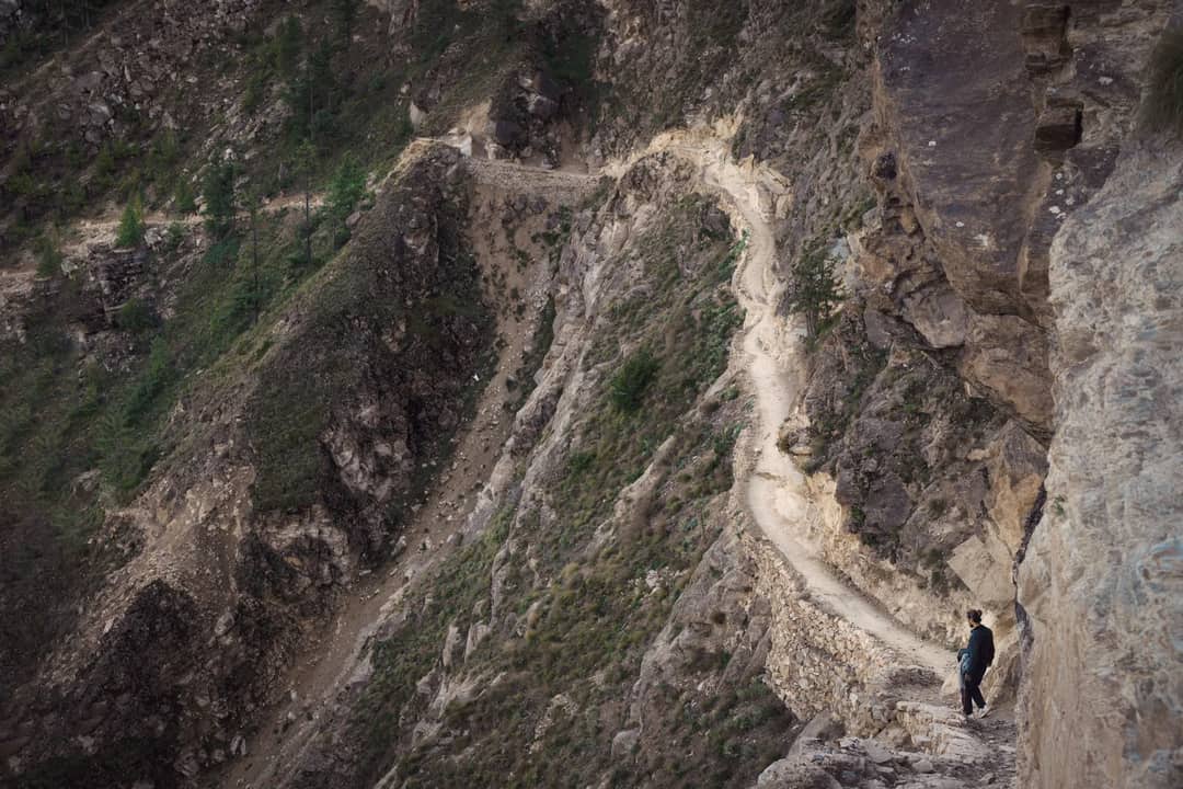 A lone hiker navigates a narrow path along rugged cliffs in Nepal, showcasing nature's raw beauty.