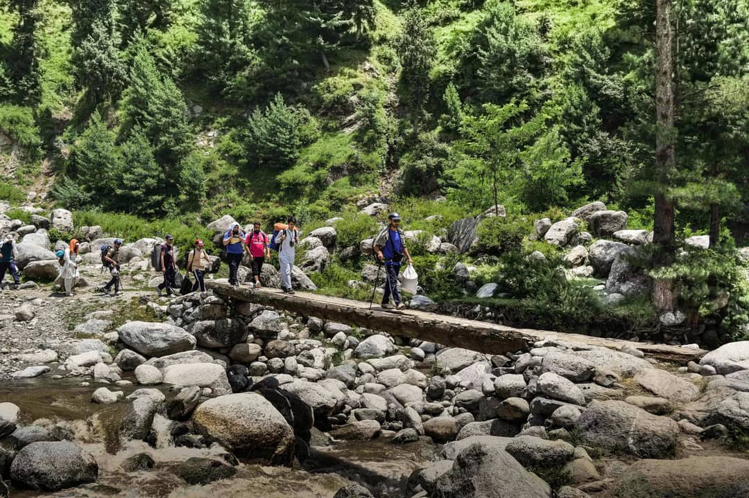 Adventurous group hiking across a wooden bridge in lush Gabin Jabba, Pakistan.