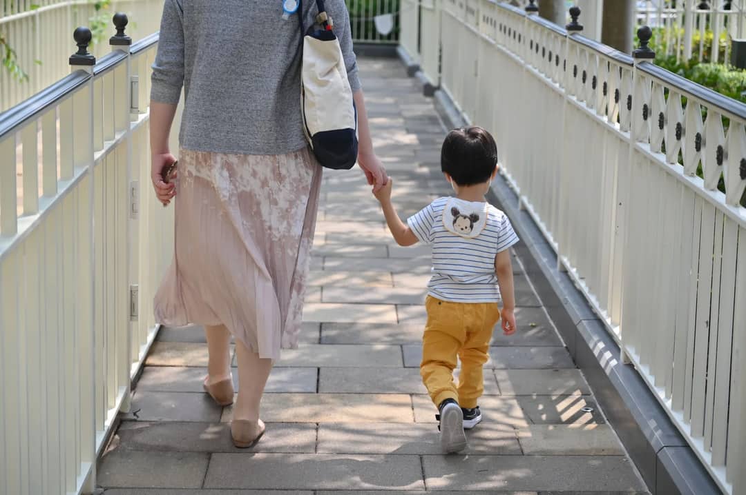 A mother and son holding hands walking on a sunlit cobblestone path.