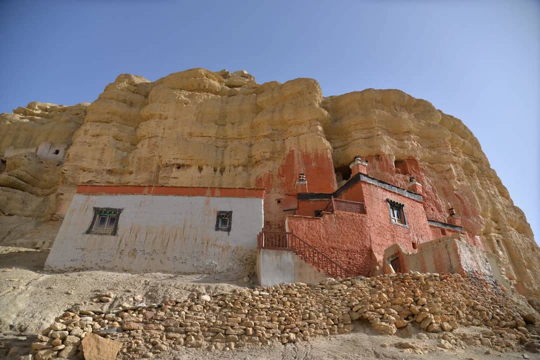 Ancient monastery built into rocky cliffs of Upper Mustang, Nepal under clear sky.