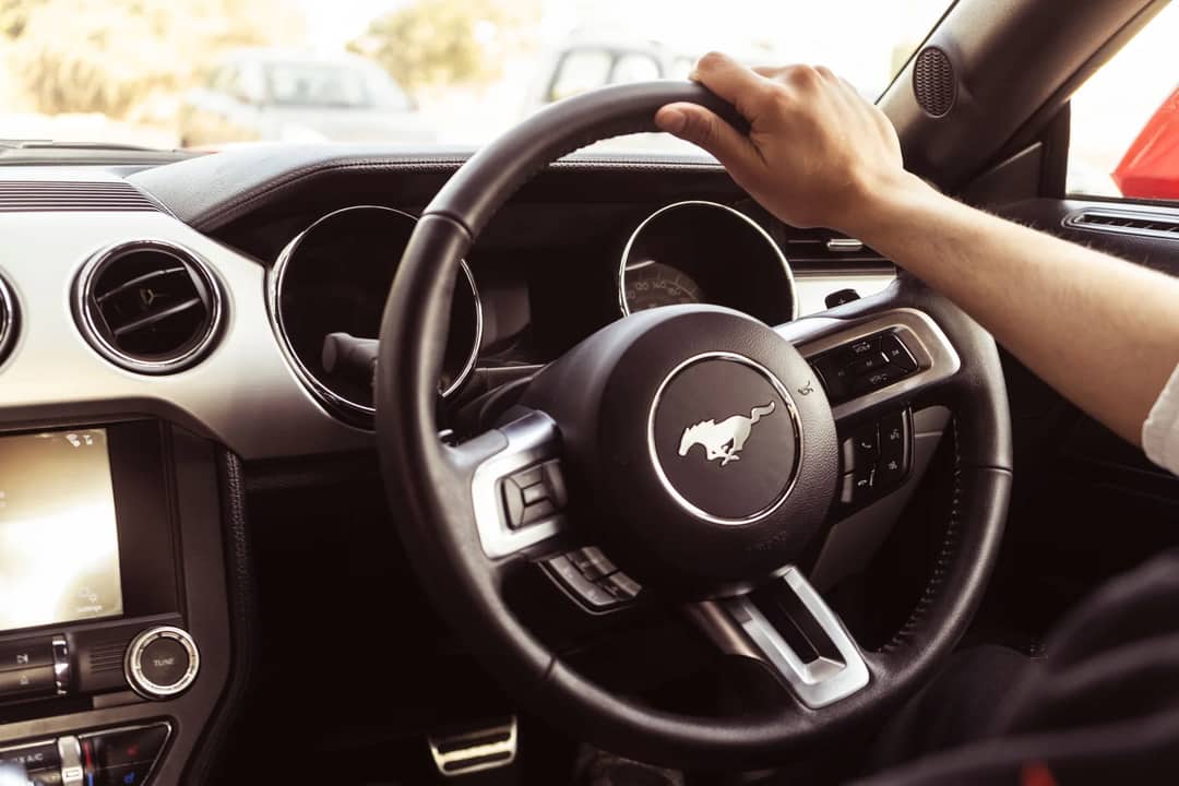 Close-up view of a car's interior featuring a hand on the steering wheel and dashboard details.