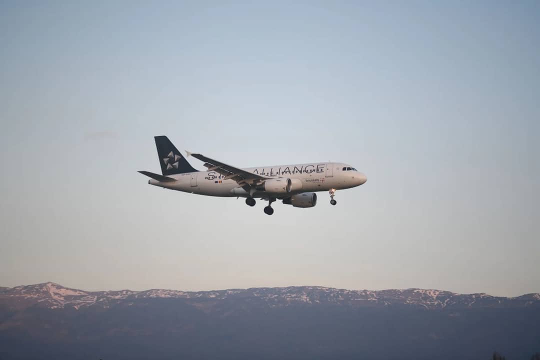 Airbus A320 aircraft descending over Geneva with a picturesque mountain backdrop at sunrise.