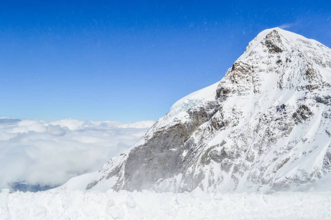 Scenery view of rough mountain with snow near clouds under blue sky in winter