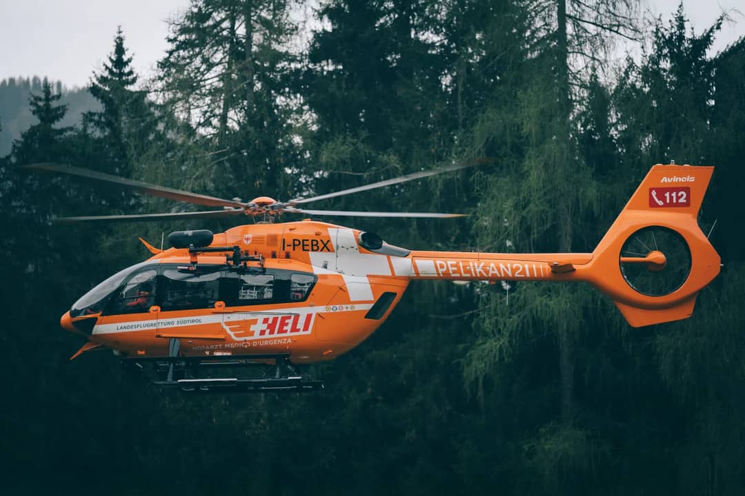 Bright orange rescue helicopter in flight over a dense forest, showcasing emergency service in action.