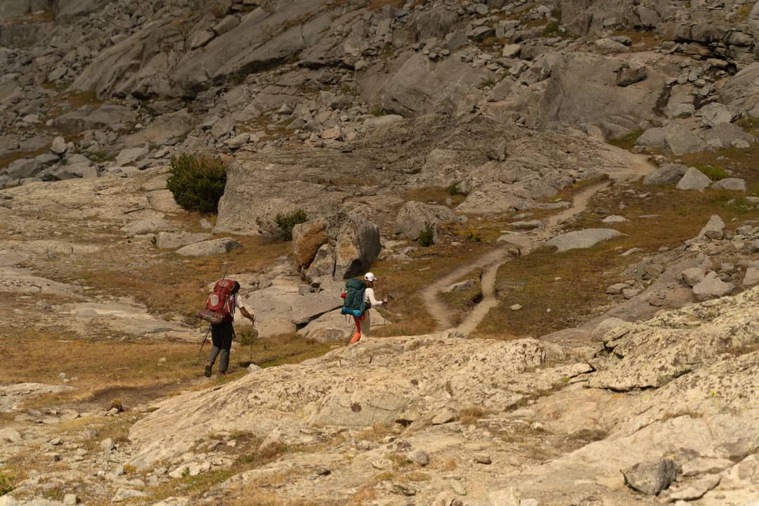 Two hikers traverse a scenic rocky trail in Wyoming's rugged landscape.