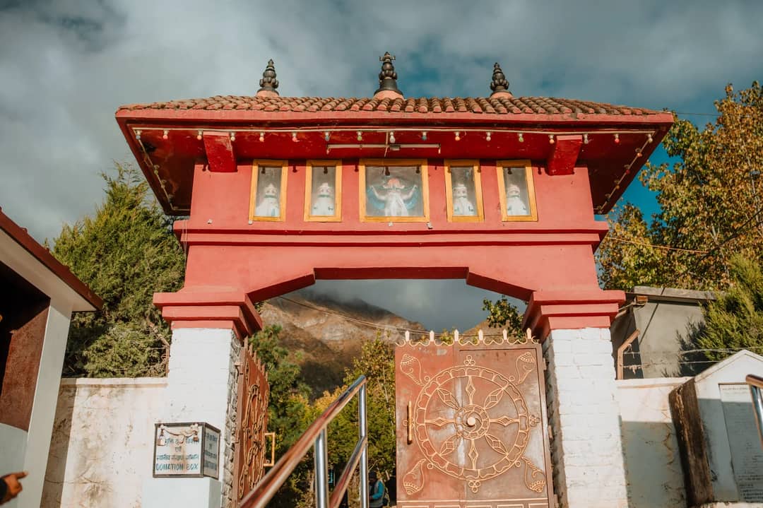 Outdoor view of a red traditional gateway with decorative gate and mountain backdrop.