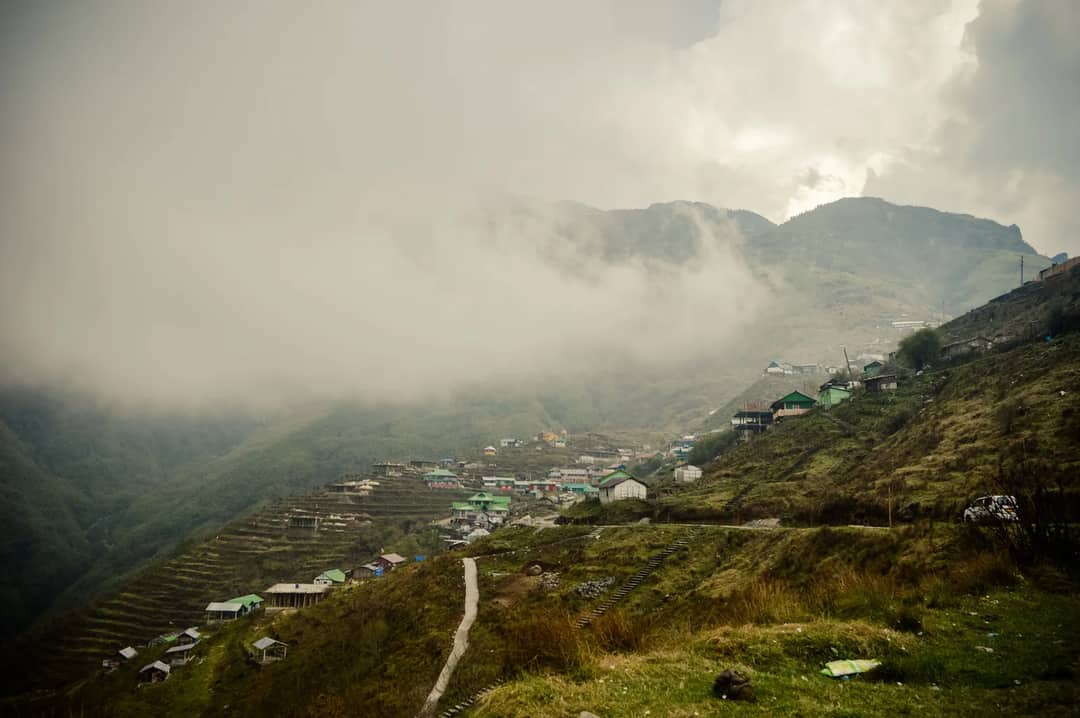 Serene landscape of a mist-covered village nestled among the hills of Sikkim, India.