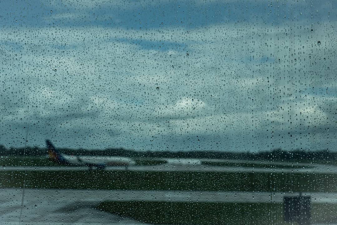 Airplane in the distance through raindrop-covered window at airport.