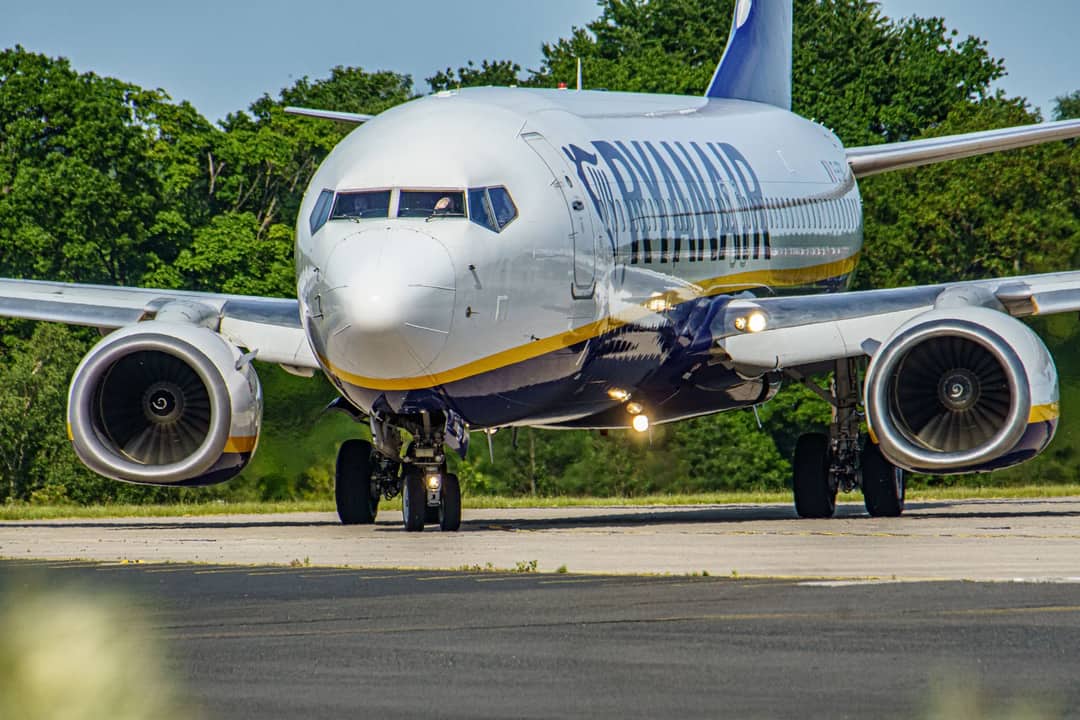 Commercial airplane taxiing on runway, surrounded by greenery, at UK airport.