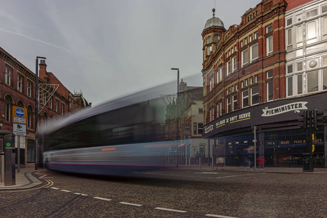 Long exposure of a bus creating motion blur in Leeds city center, highlighting historic architecture.