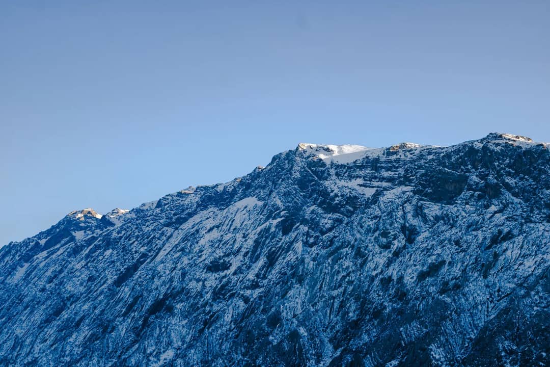 Stunning view of snow-covered rocky mountain peaks against a clear blue sky, showcasing winter's beauty and rugged terrain.