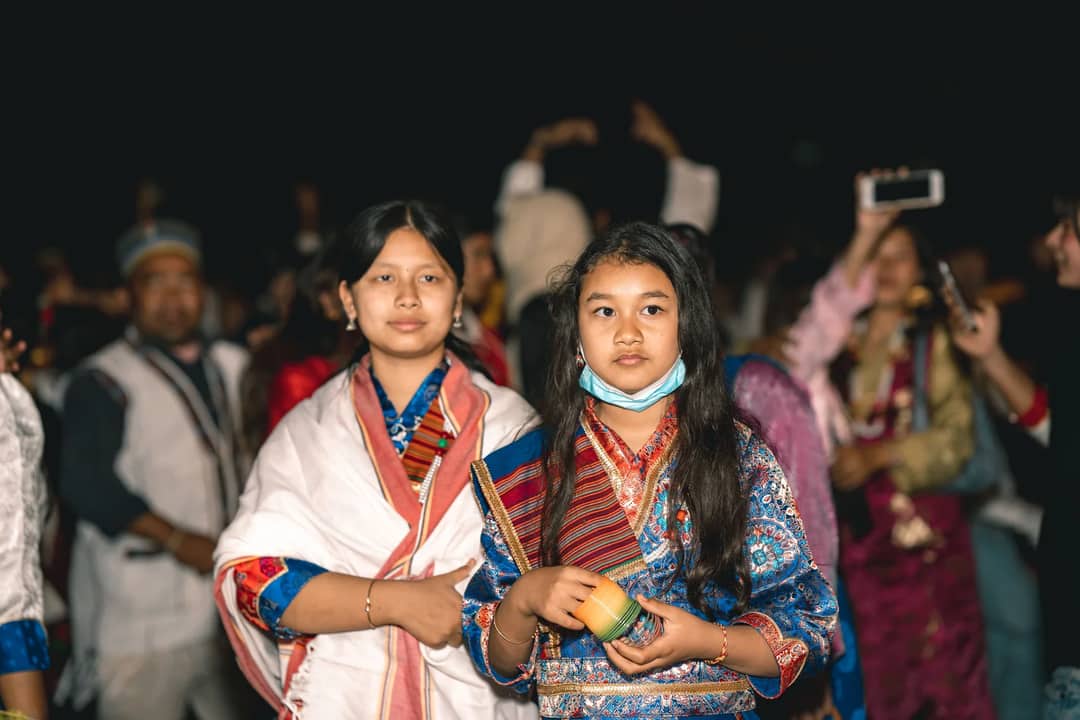 Women in vibrant traditional costumes at a lively outdoor folk festival during the night.