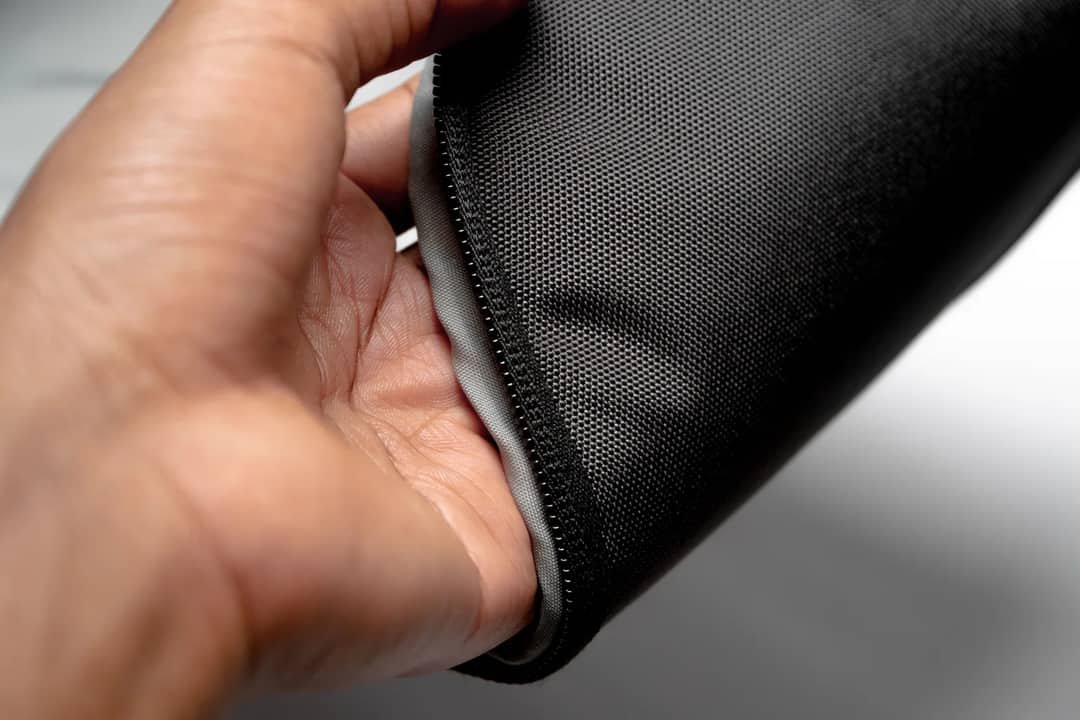 A hand holding the zipped edge of a soft-sided bag — the zips, wheels and handle fail long before the shell does