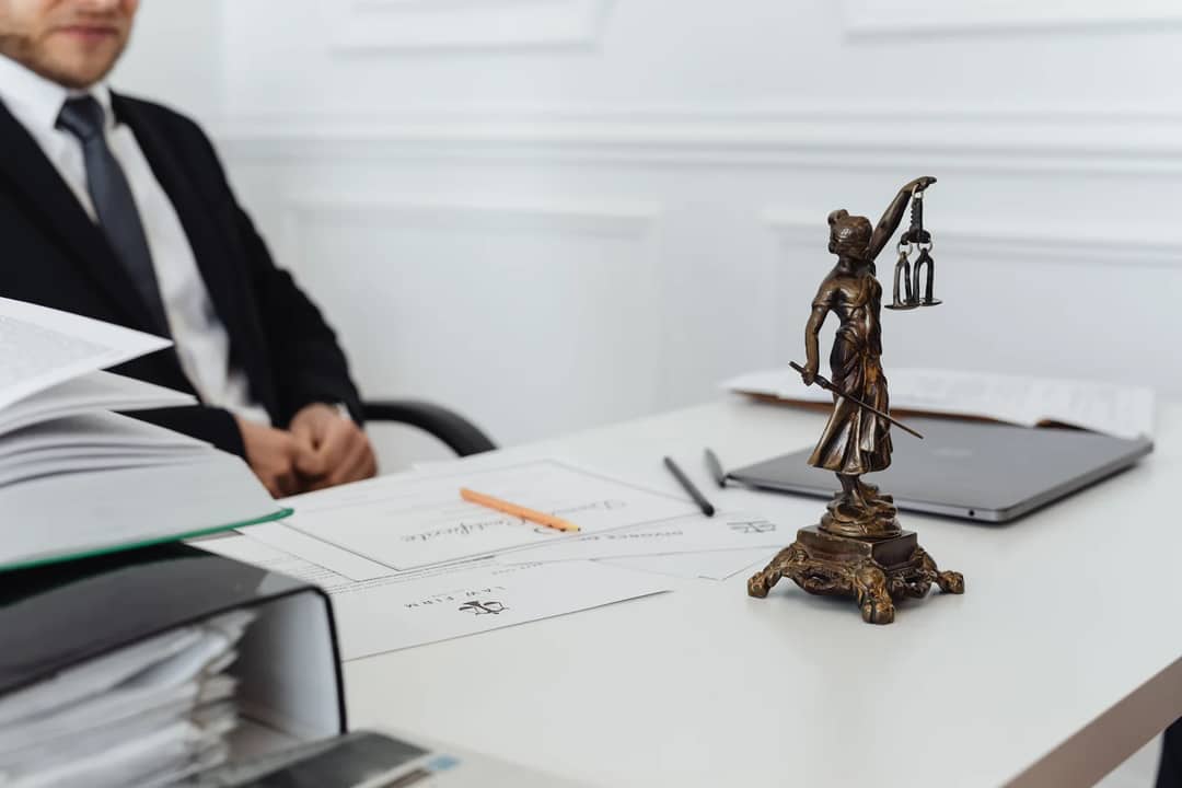 A lawyer at a desk beside a figure of the scales of justice
