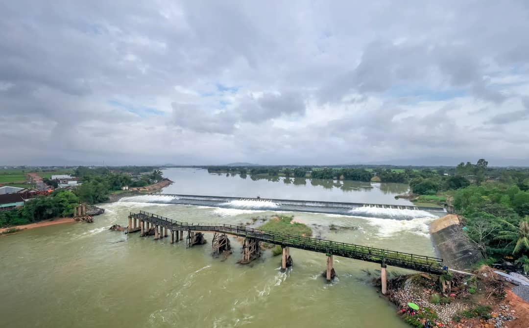 Drone shot of a damaged bridge over a river under a cloudy sky.