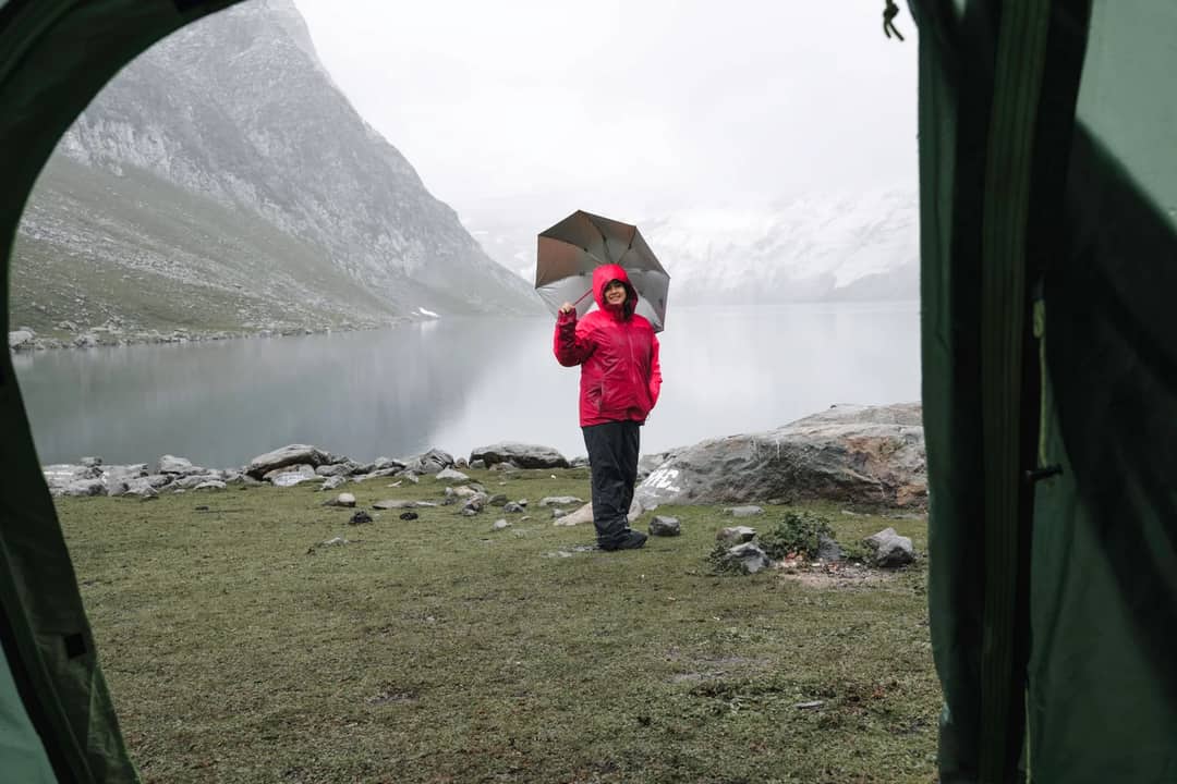 Cheerful woman with umbrella in scenic mountainous campsite by the lake with a tent view.