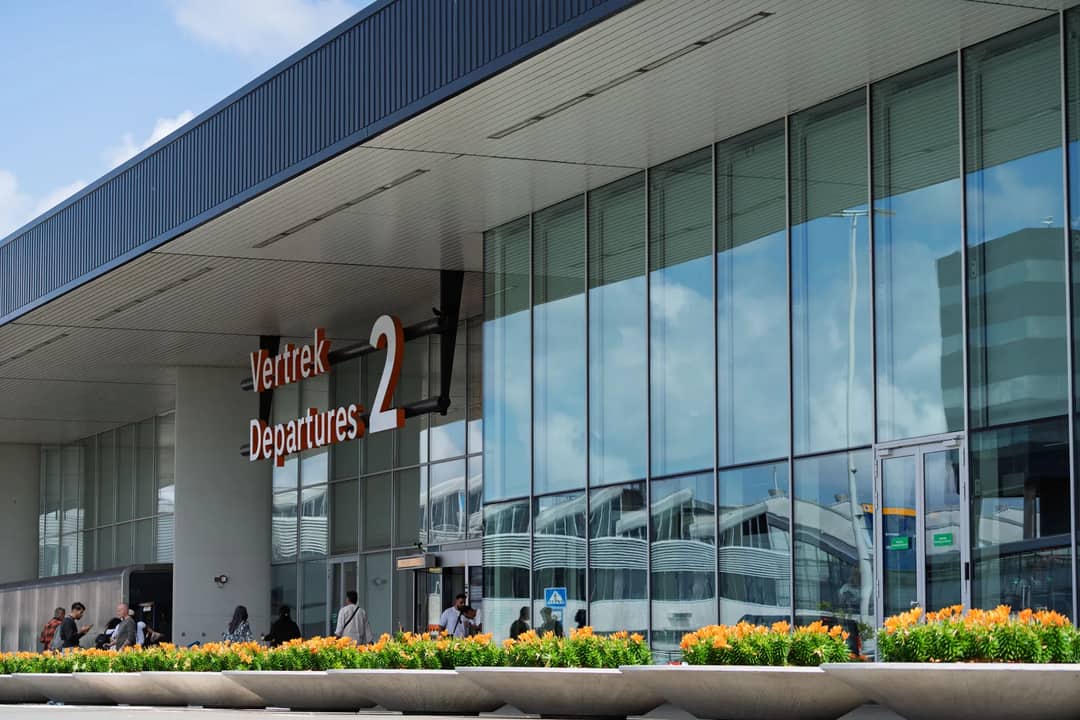 Glass facade of a bustling airport departure terminal with people outside and reflection of clouds.
