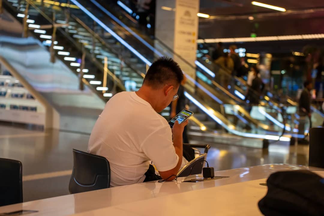 Adult using smartphone in modern airport terminal, Doha, Qatar. Busy travel scene with escalator.