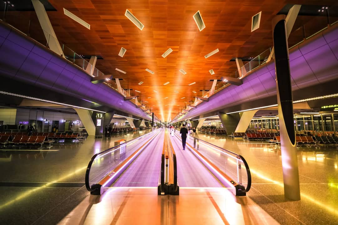 Long exposure shot of a vibrant airport terminal with moving walkway and colorful lighting.