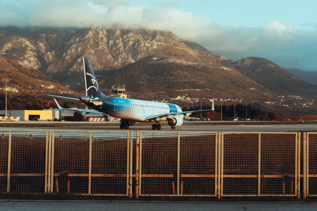 Airplane at Tivat Airport surrounded by stunning Montenegrin mountains during daylight.