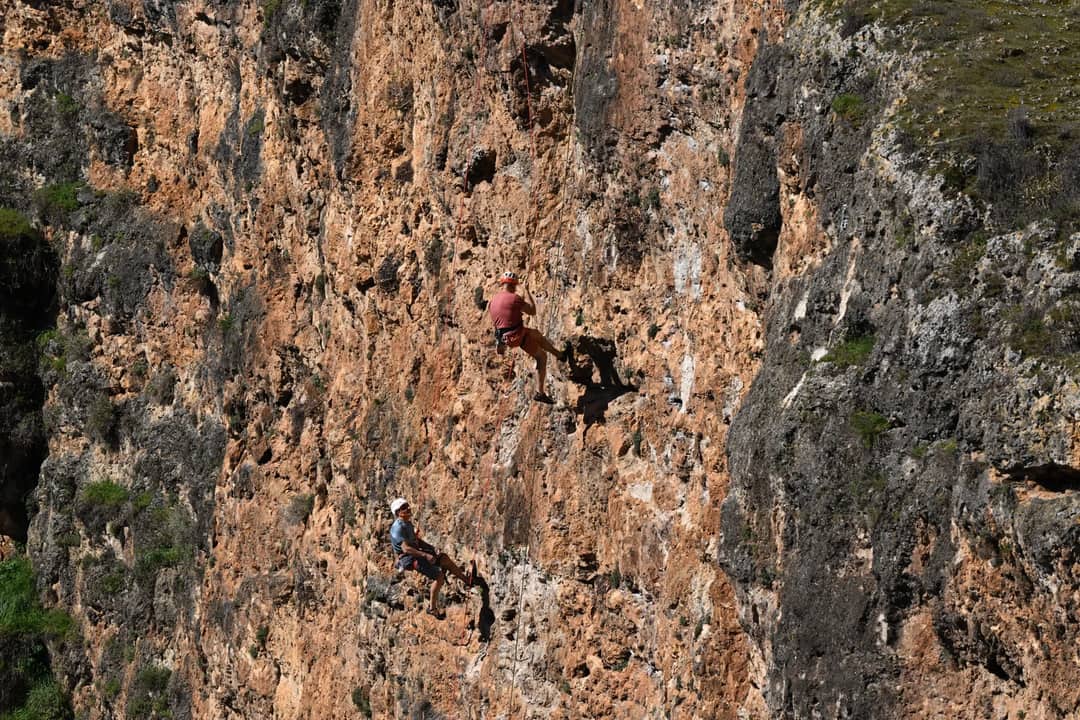 Two climbers scale a steep rocky cliff in bright daylight, showcasing adventure and skill.