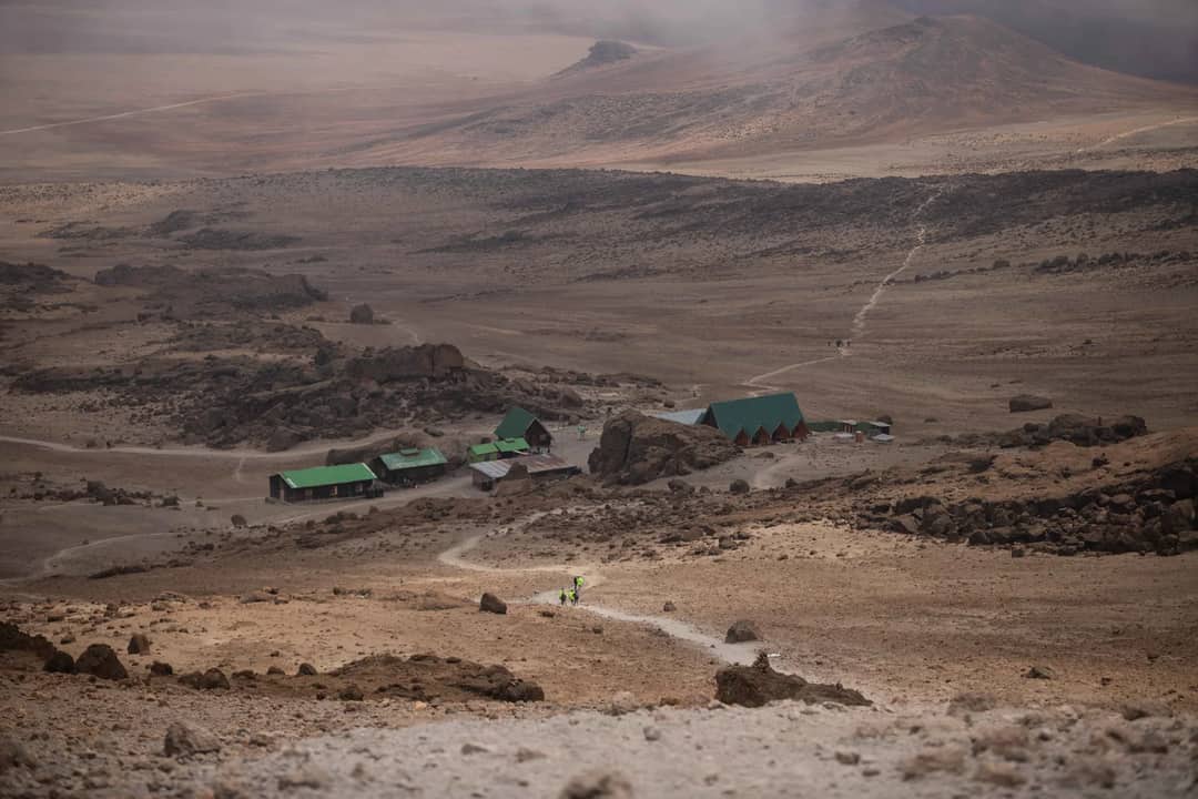 High-angle shot of hikers approaching a remote mountain base camp with rugged terrain.