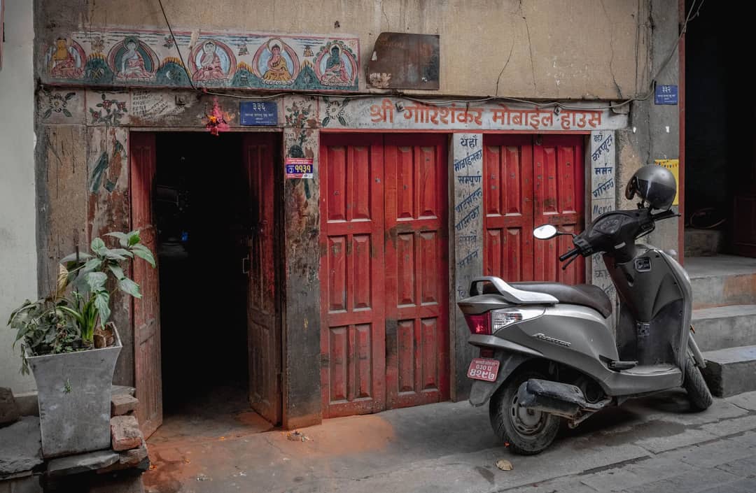 A traditional building with red doors and a parked scooter in Kathmandu, Nepal streets.