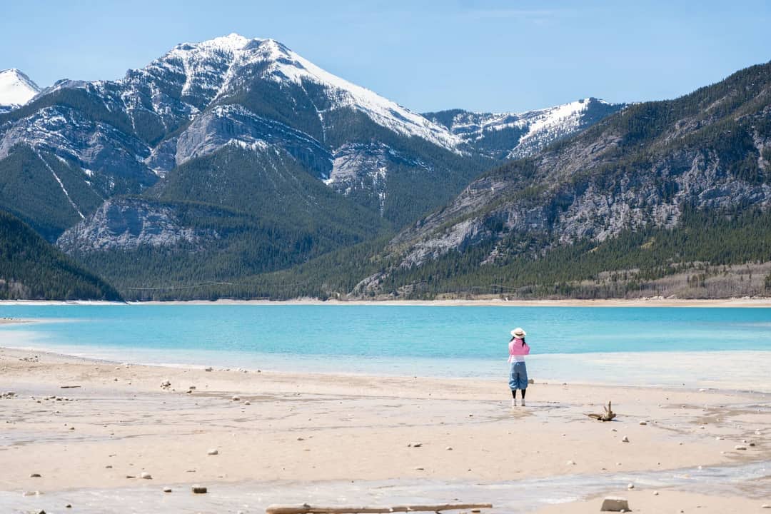 A lone woman stands at Barrier Lake, Kananaskis, with majestic mountains in the background.