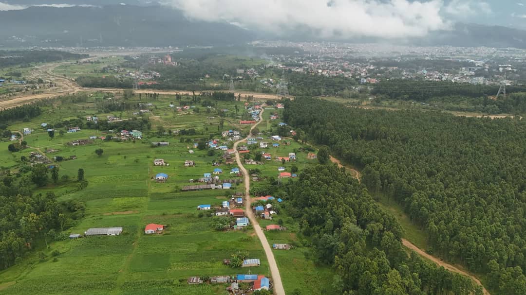 Aerial shot showcasing a sprawling village and lush greenery under clouded skies in Nepal.