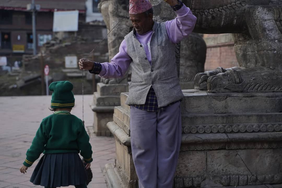 An elderly man and a child in a Nepalese town, interacting by ancient stone sculpture.