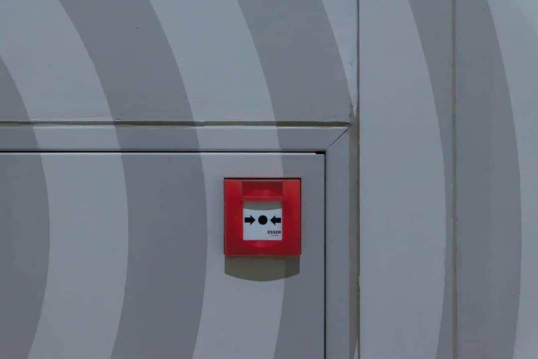Red emergency button on a grey patterned wall, emphasizing safety measures.