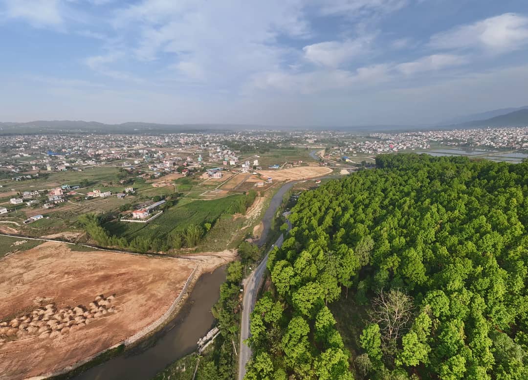 A scenic aerial view showcasing lush green forests alongside an expanding city under the bright sky.