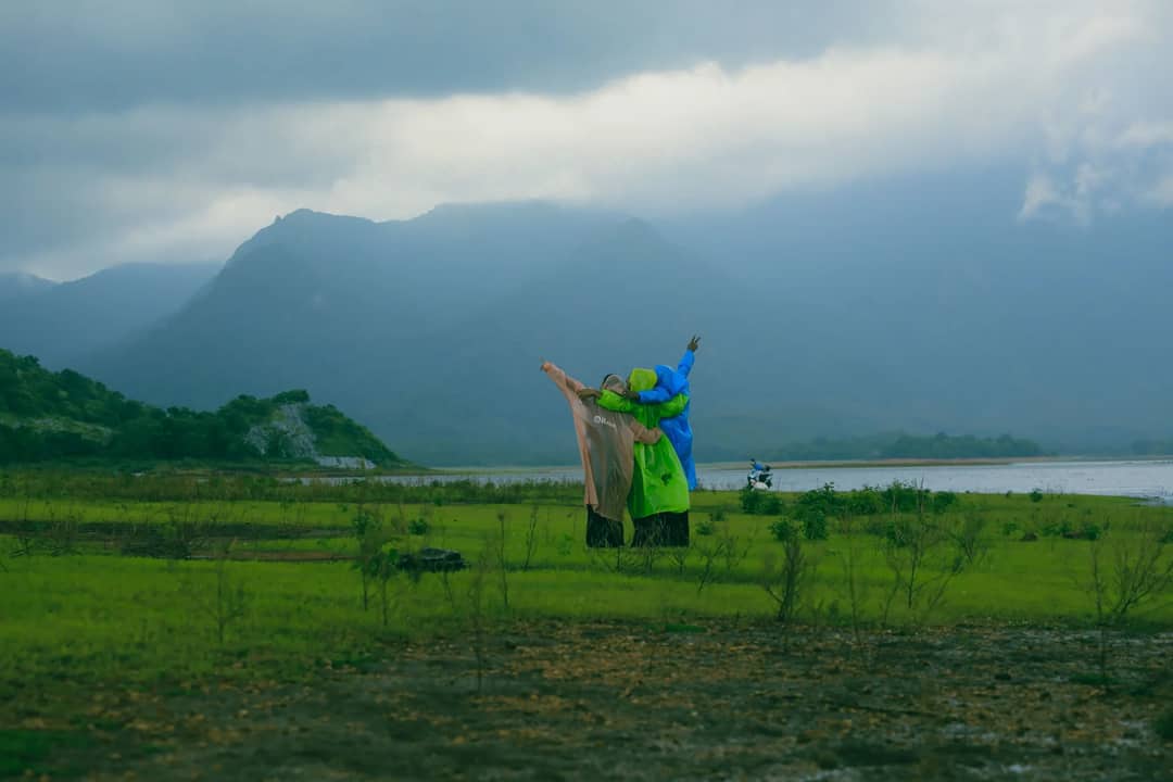 Group of people wearing colorful raincoats enjoying the view by a lake with mountains in the background.