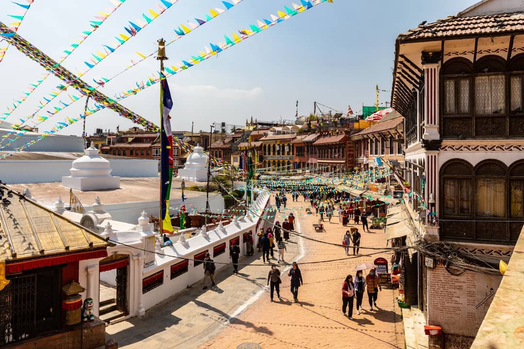 Colorful flags and lively streets around Boudhanath Stupa in Kathmandu, Nepal, with bustling activity.