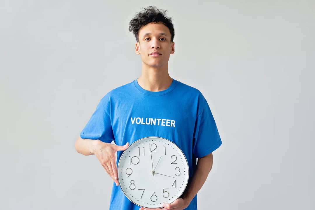 Young male volunteer in blue shirt holding a clock, symbolizing time management.