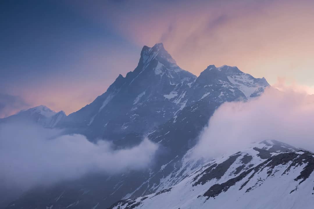 Stunning view of a snow-capped Himalayan mountain peak surrounded by clouds at sunset.