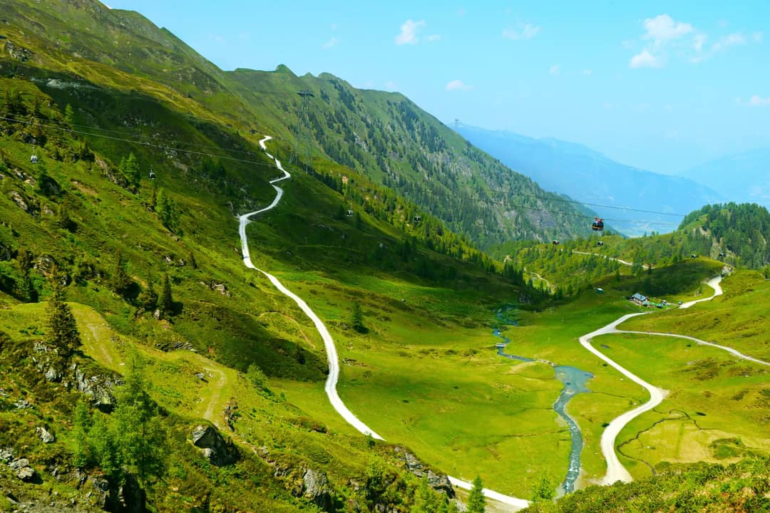 A trail winding up a green mountain valley above a river