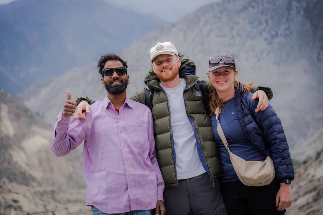Three friends enjoying a scenic view in Lo Manthang, Nepal, with a mountainous backdrop.