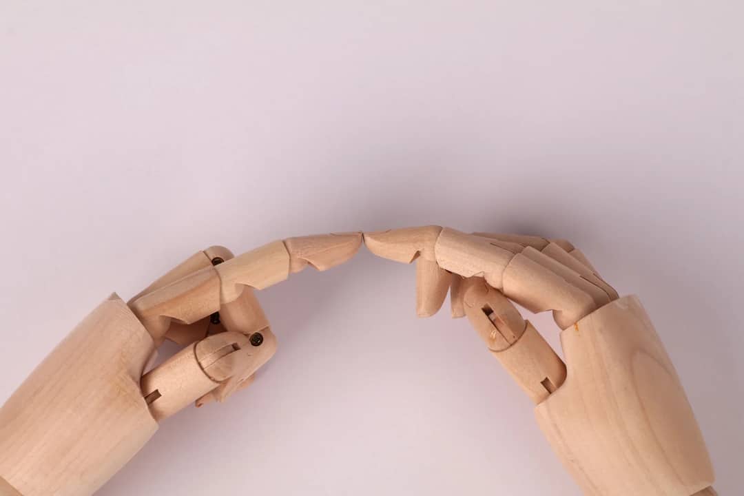 Close-up of wooden mannequin hands almost touching, capturing a concept of connection.