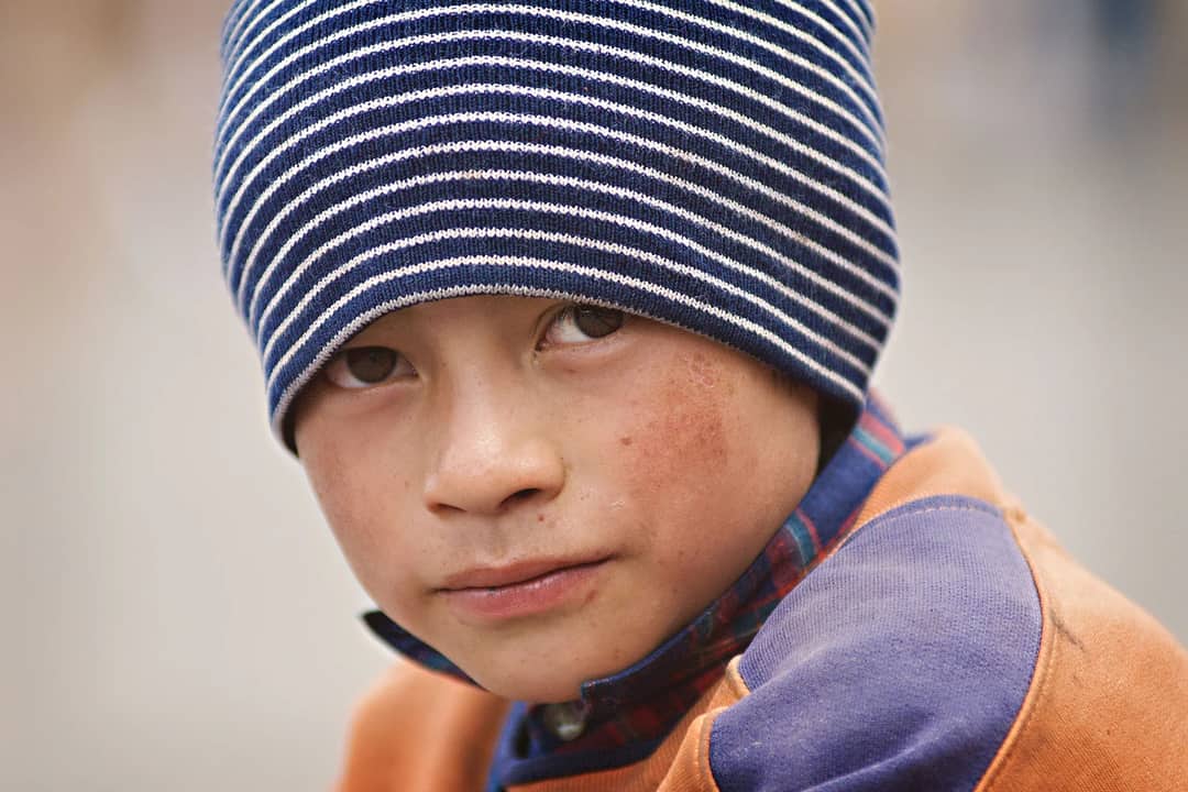 A close-up portrait of a young boy wearing a striped beanie, looking thoughtfully into the camera.