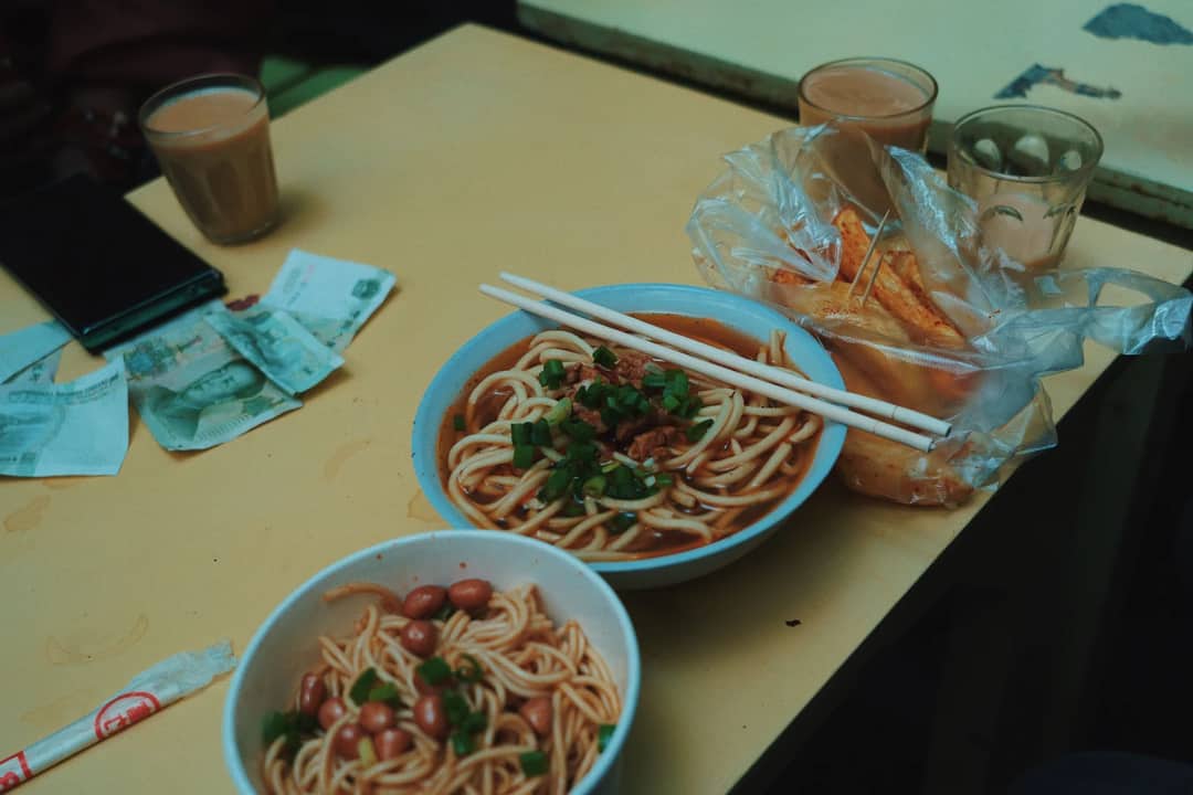 High-angle view of an authentic Asian meal with noodles, tea, and chopsticks on a wooden table.