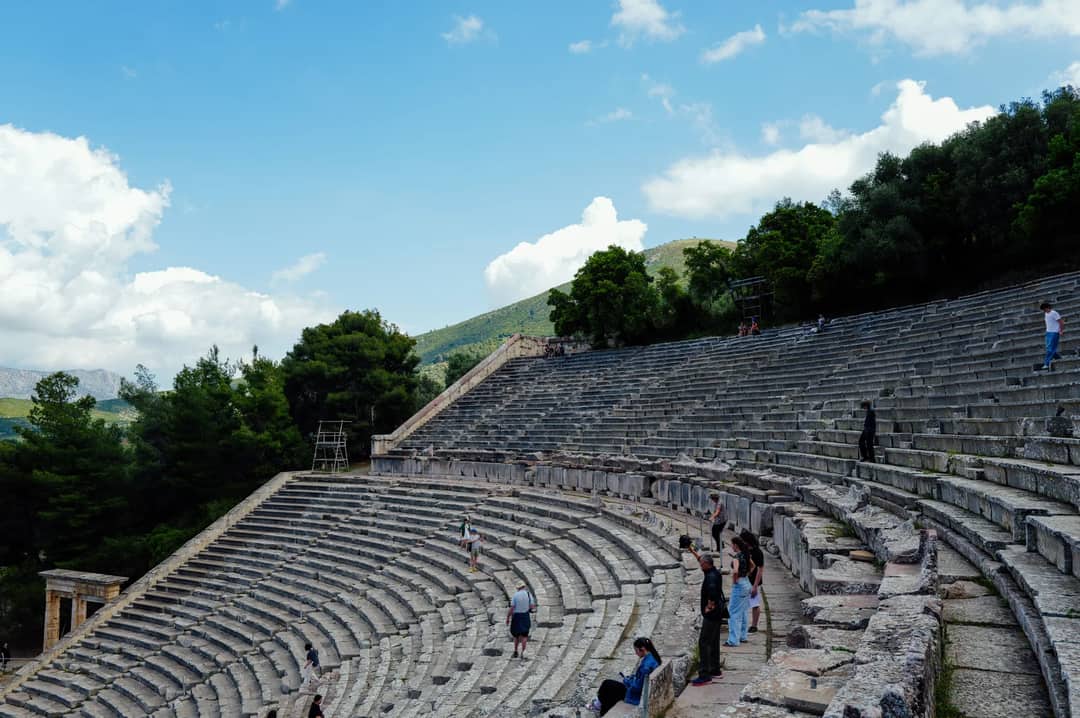 View of the Ancient Theater of Epidaurus with tourists wandering and capturing photos.