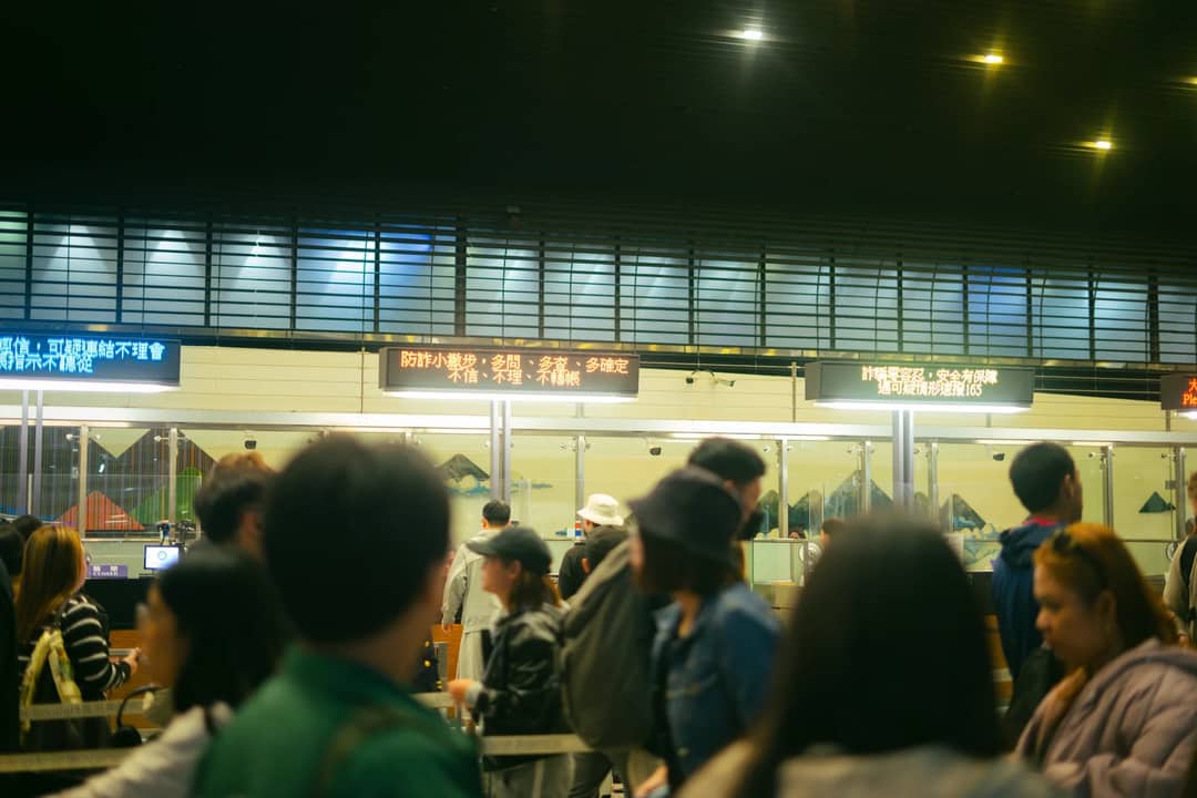Crowded airport check-in area with people queueing and visible flight information signs.
