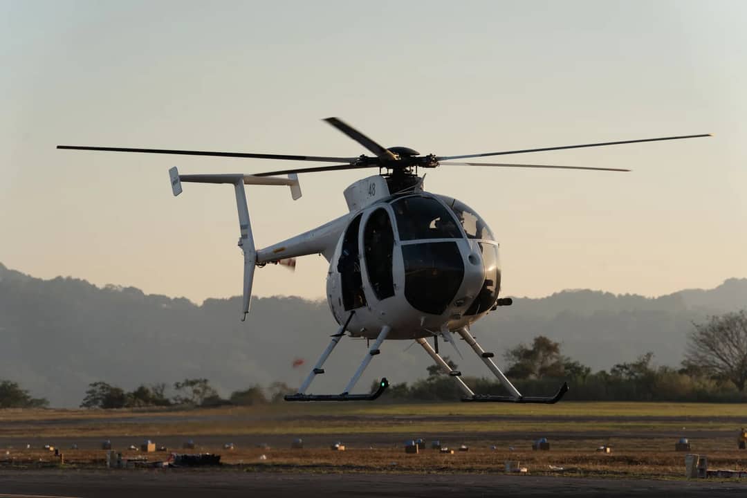 A helicopter hovering just above the ground at Ilopango Airport in El Salvador during daylight.