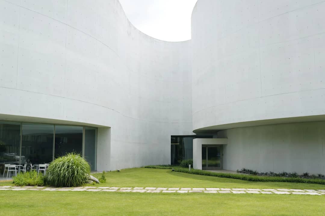 Contemporary building design with green landscaping, featuring curved concrete surfaces.