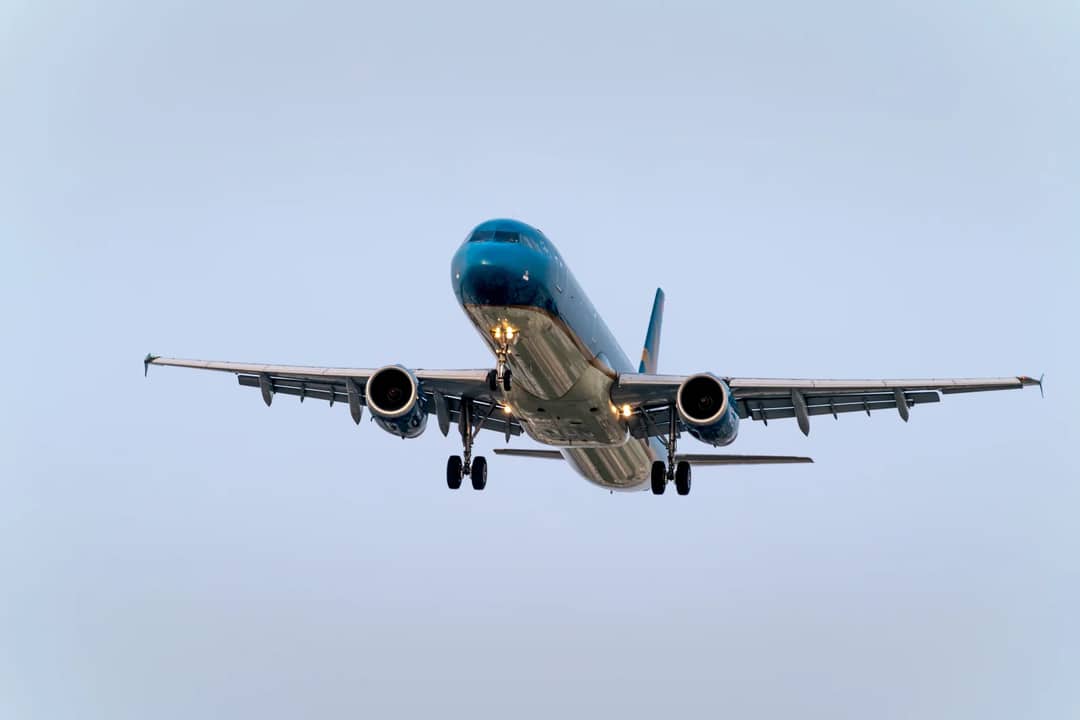 A large commercial airplane flying low in the sky, showing a clear blue background.