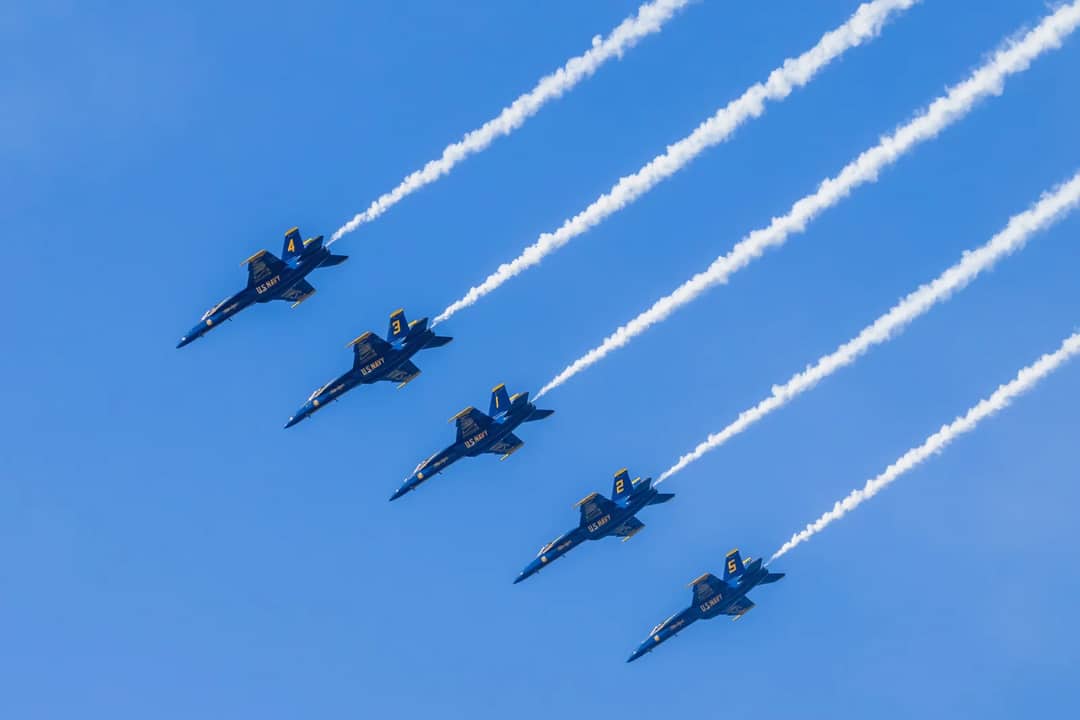 US Navy fighter jets in synchronized aerial performance against a clear blue sky.